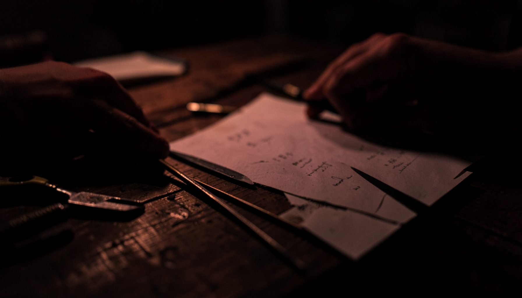 A close view of hand tools and paper arranged on a dark wooden table with warm low shadow