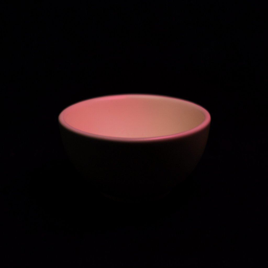 A small dark square photo of a cream ceramic bowl with faint pink light